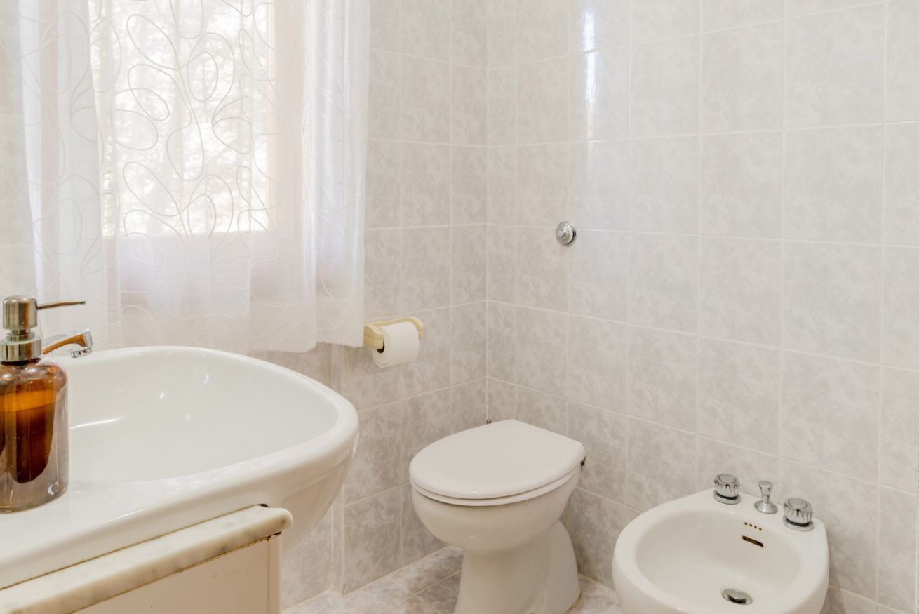 A bathroom with a sink, toilet, bidet, and a window with a curtain.