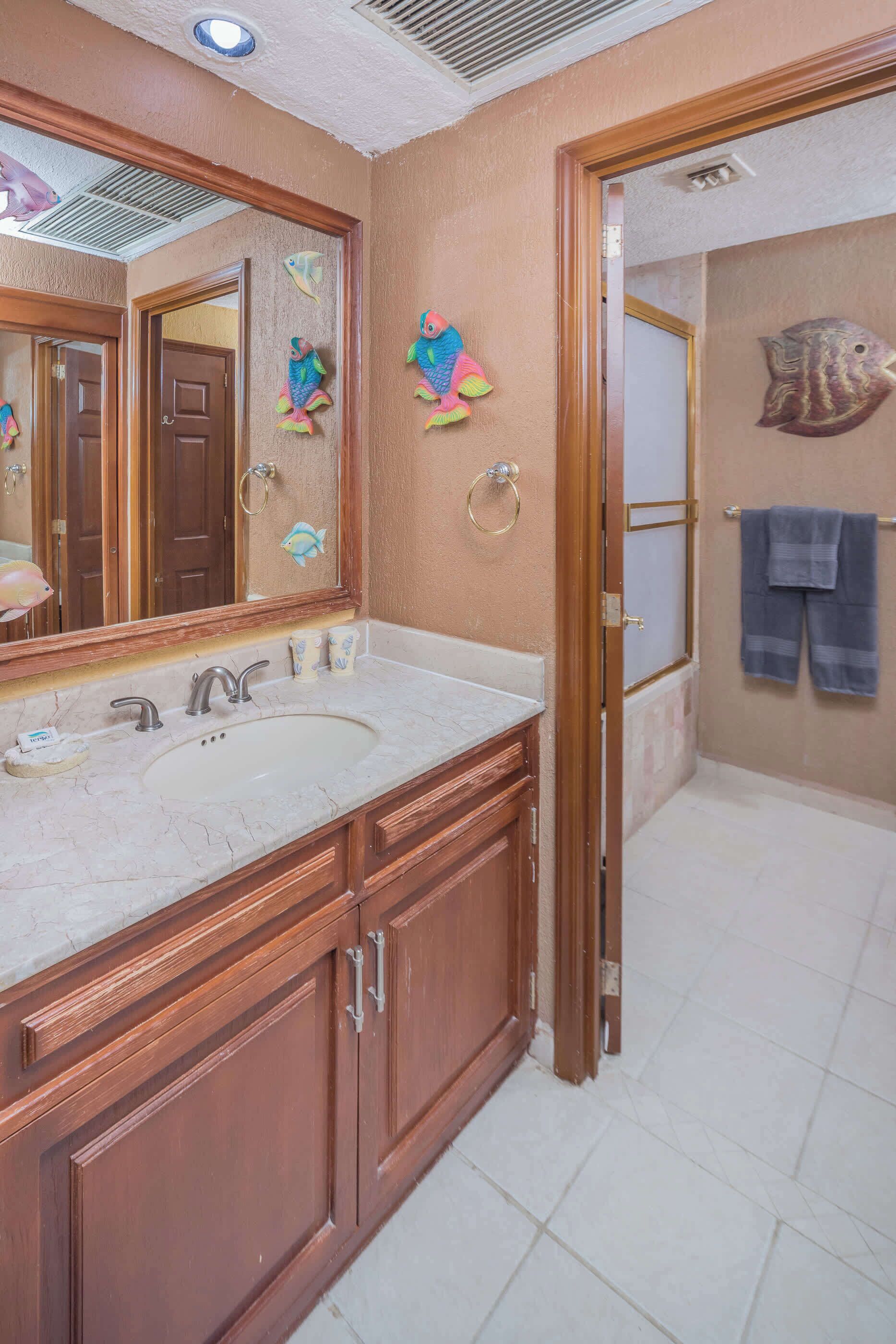 A bathroom with wooden cabinets, a marble sink, and decorative fish wall art.