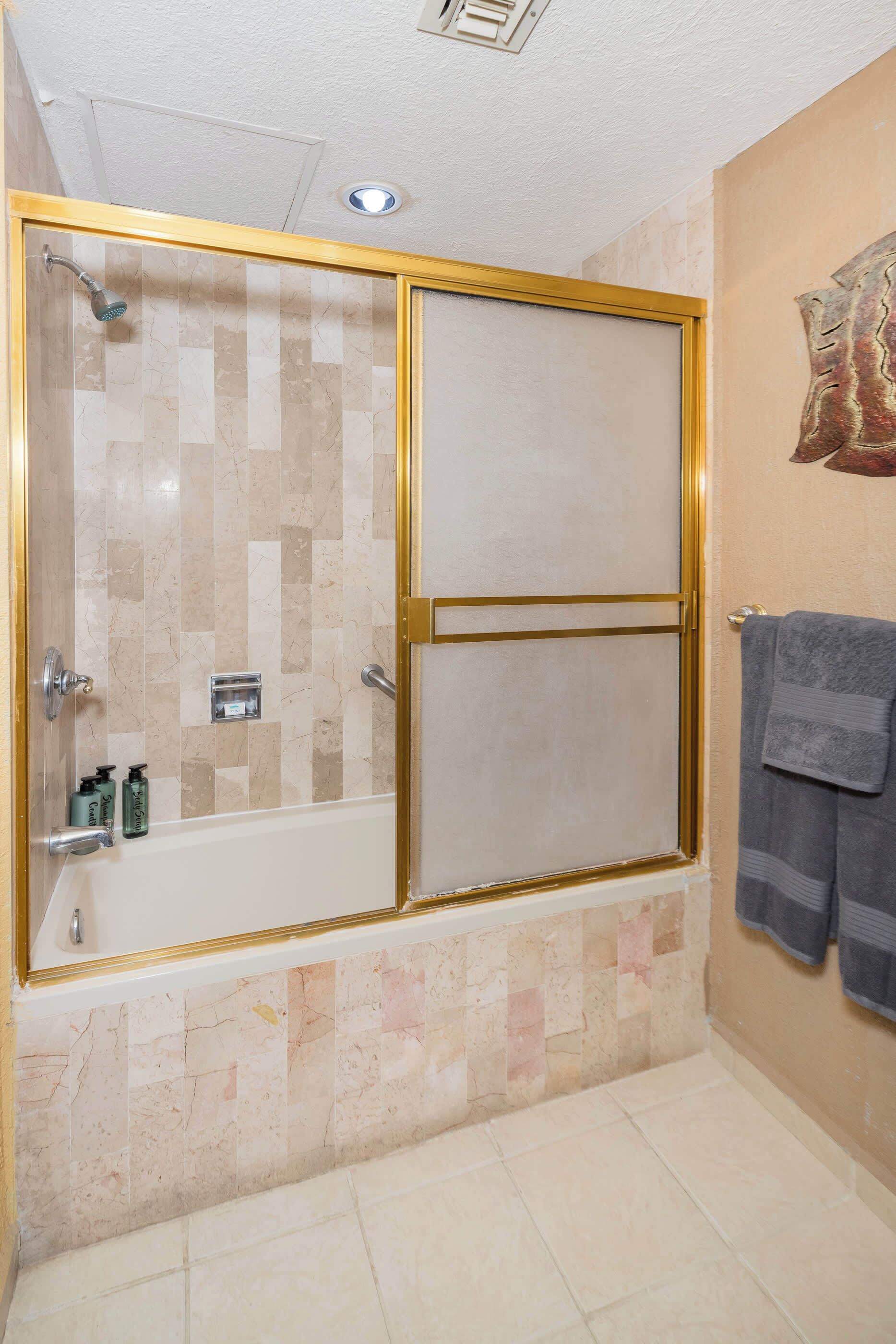 Baño con ducha a nivel, baldosas de mármol, un perchero y una lámpara en el techo.
