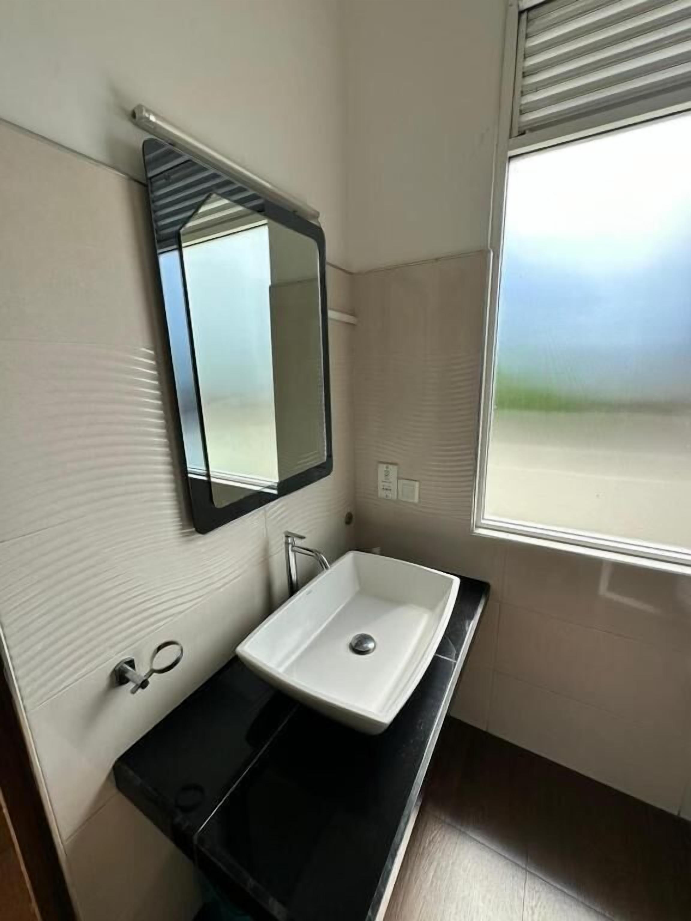A bathroom with a white sink, a mirror, and a window with blinds.