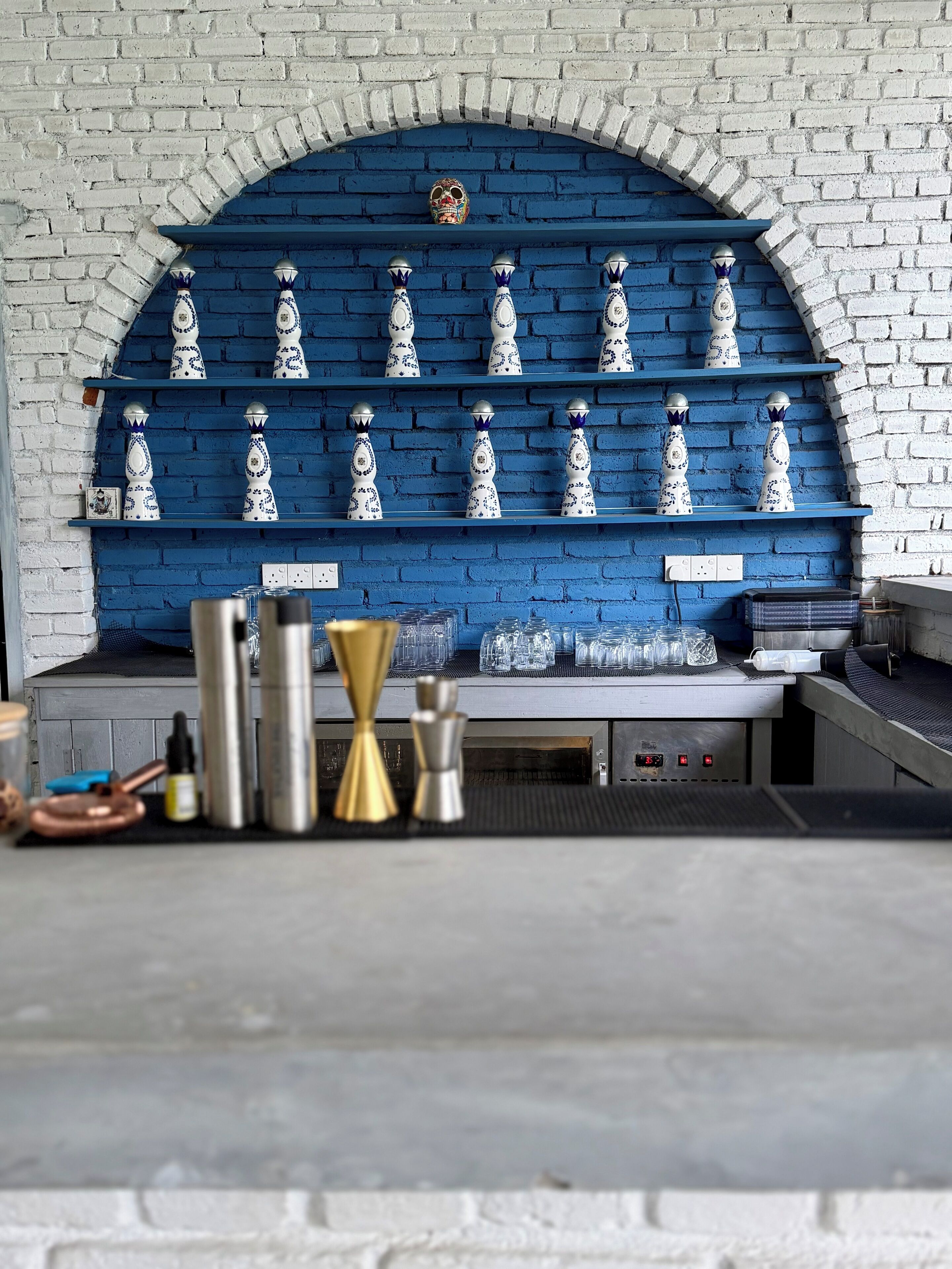 A bar area with shelves of decorative vases and a variety of bar tools on the counter.