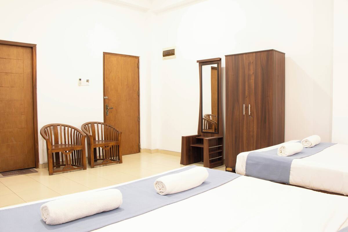 A hotel room with two beds, wooden furniture, a mirror, and a small seating area.