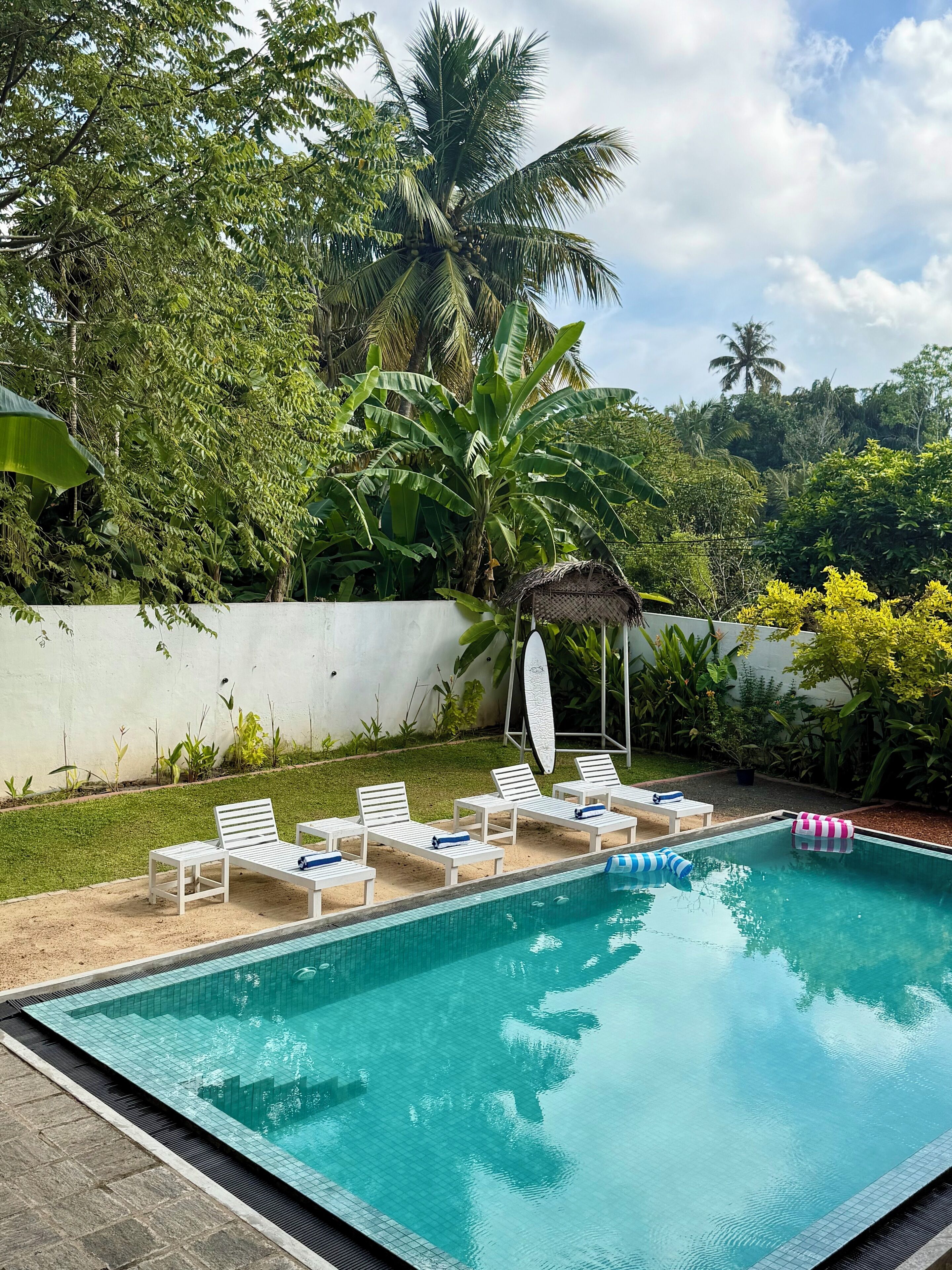 A swimming pool with white lounge chairs and a thatched-roof structure.