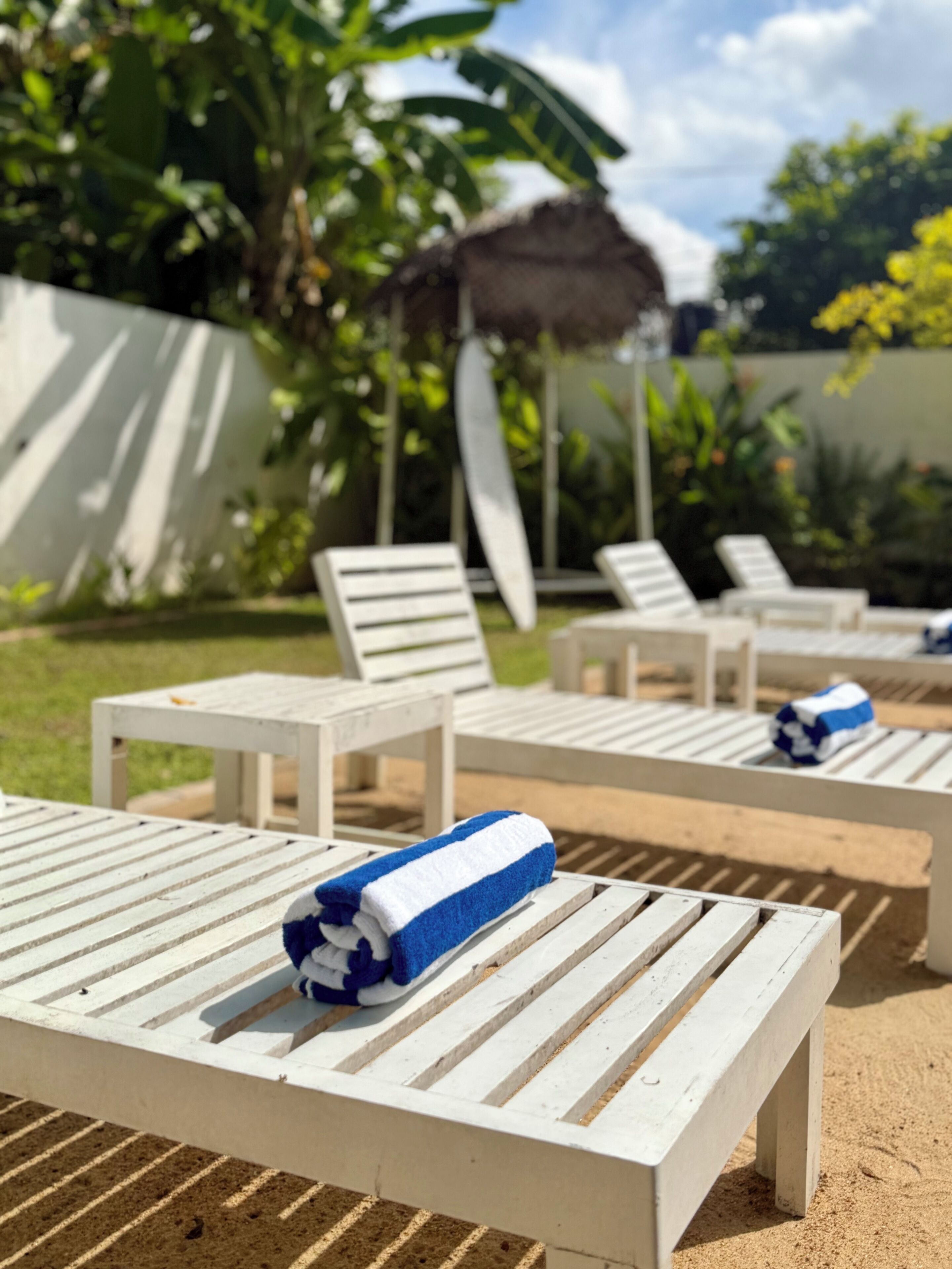 Outdoor lounge chairs with towels, a thatched roof structure, and lush greenery in the background.