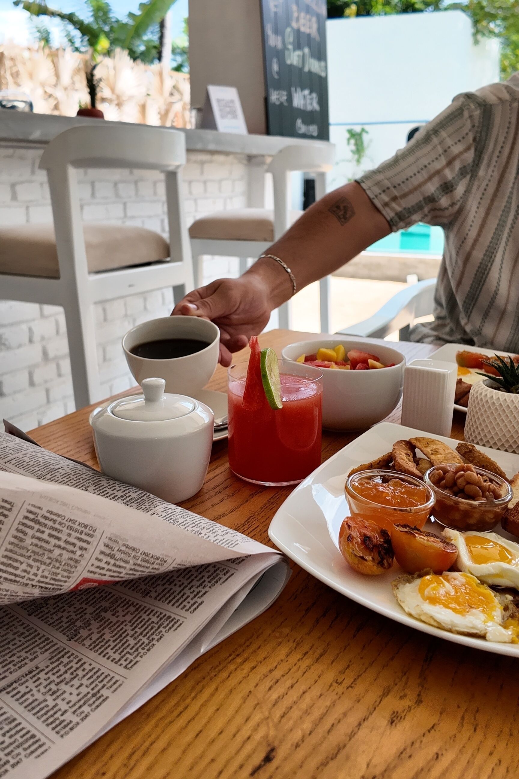 A breakfast table with a newspaper, coffee cup, fruit bowl, and a plate with eggs and toast.