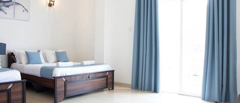 A hotel room with two beds, a large window with curtains, and a wall-mounted light fixture.