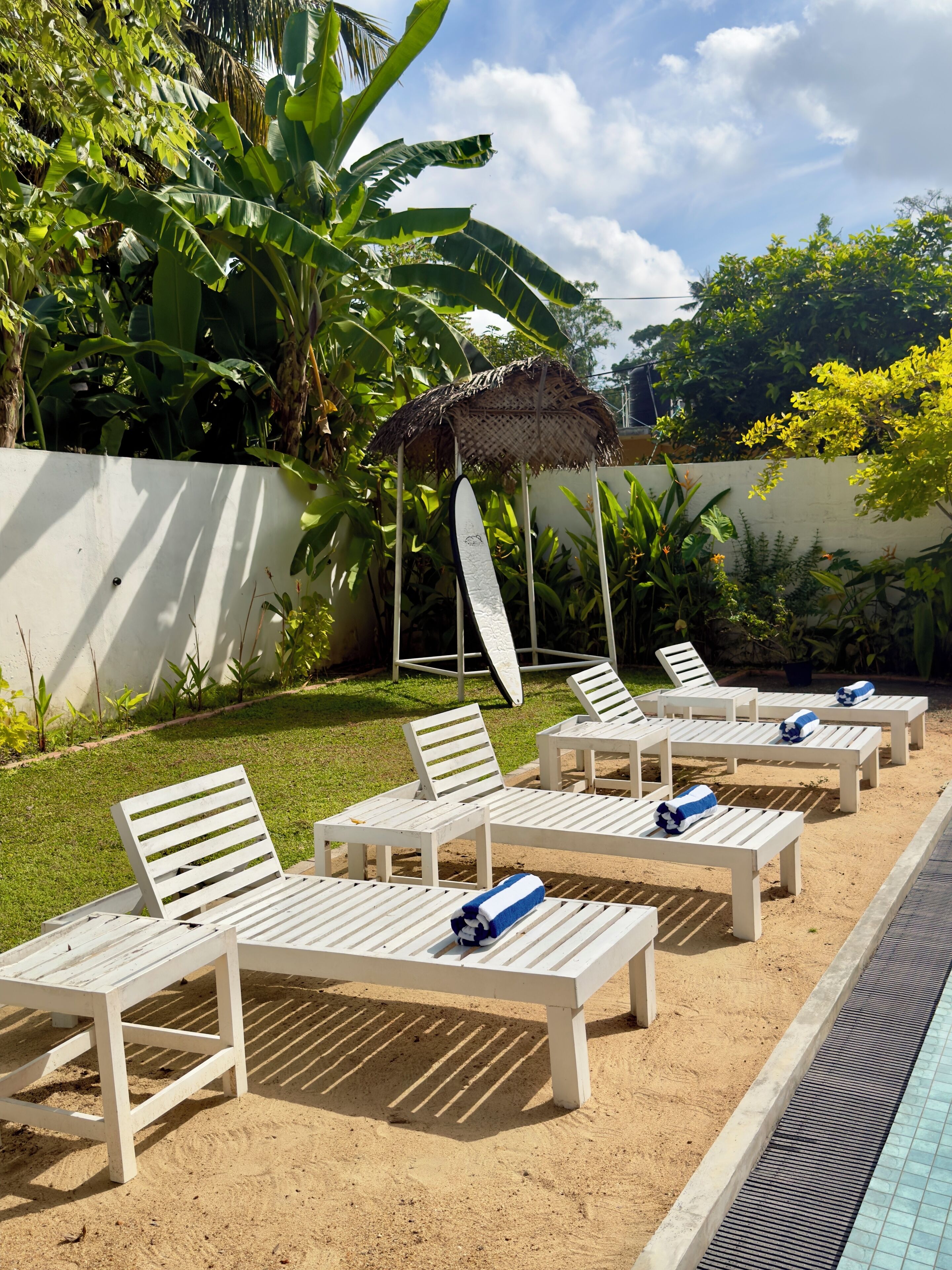 A poolside area with white lounge chairs and a thatched umbrella.