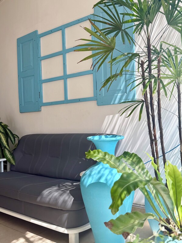 A room with a grey sofa, a blue wall-mounted shutter, and a large potted plant. - Coastal Retreat Mirissa (Mirissa)