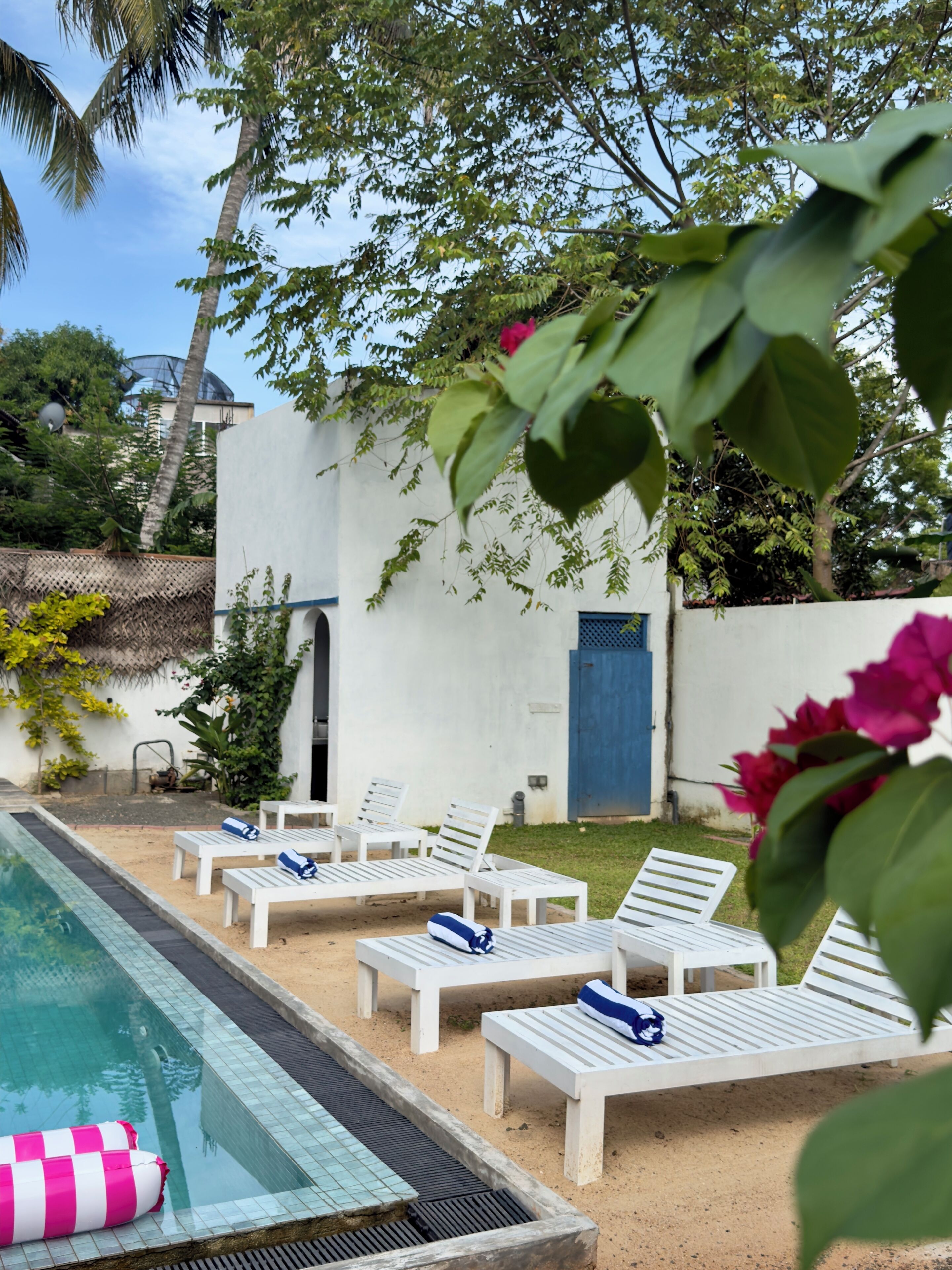 A pool area with white lounge chairs and a pink and white inflatable float.