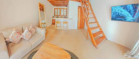 A living room with a sofa, coffee table, and a wooden staircase leading to a kitchen area.