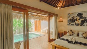 A bedroom with a large bed, a sofa, a small table, and a view of a pool. - RATU Village – Luxury Island Apartment & Private Villa Gili Air (Gili Air)