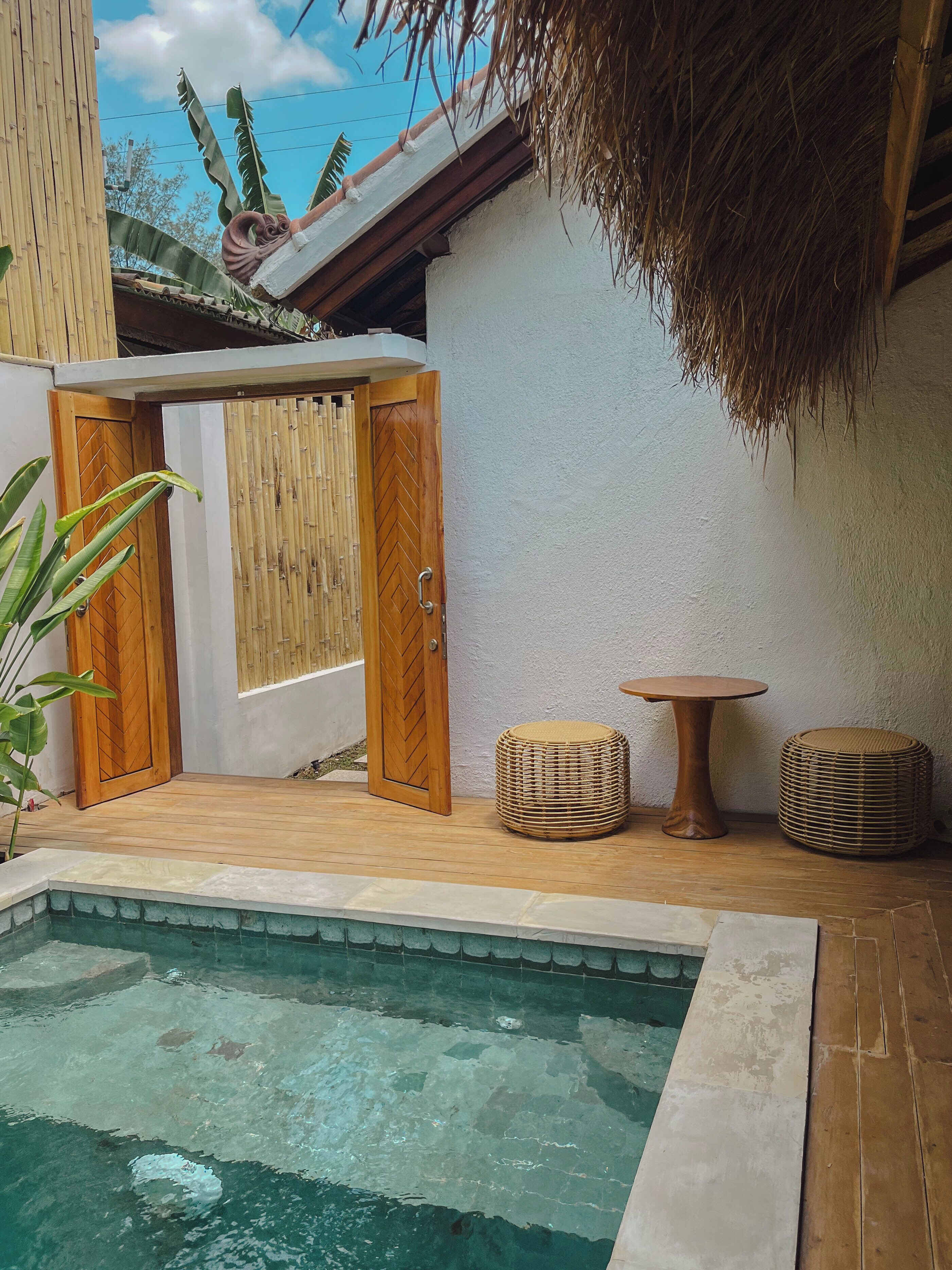 Ein Poolbereich mit Holzterrasse, einem kleinen runden Tisch und zwei Korbstühlen.