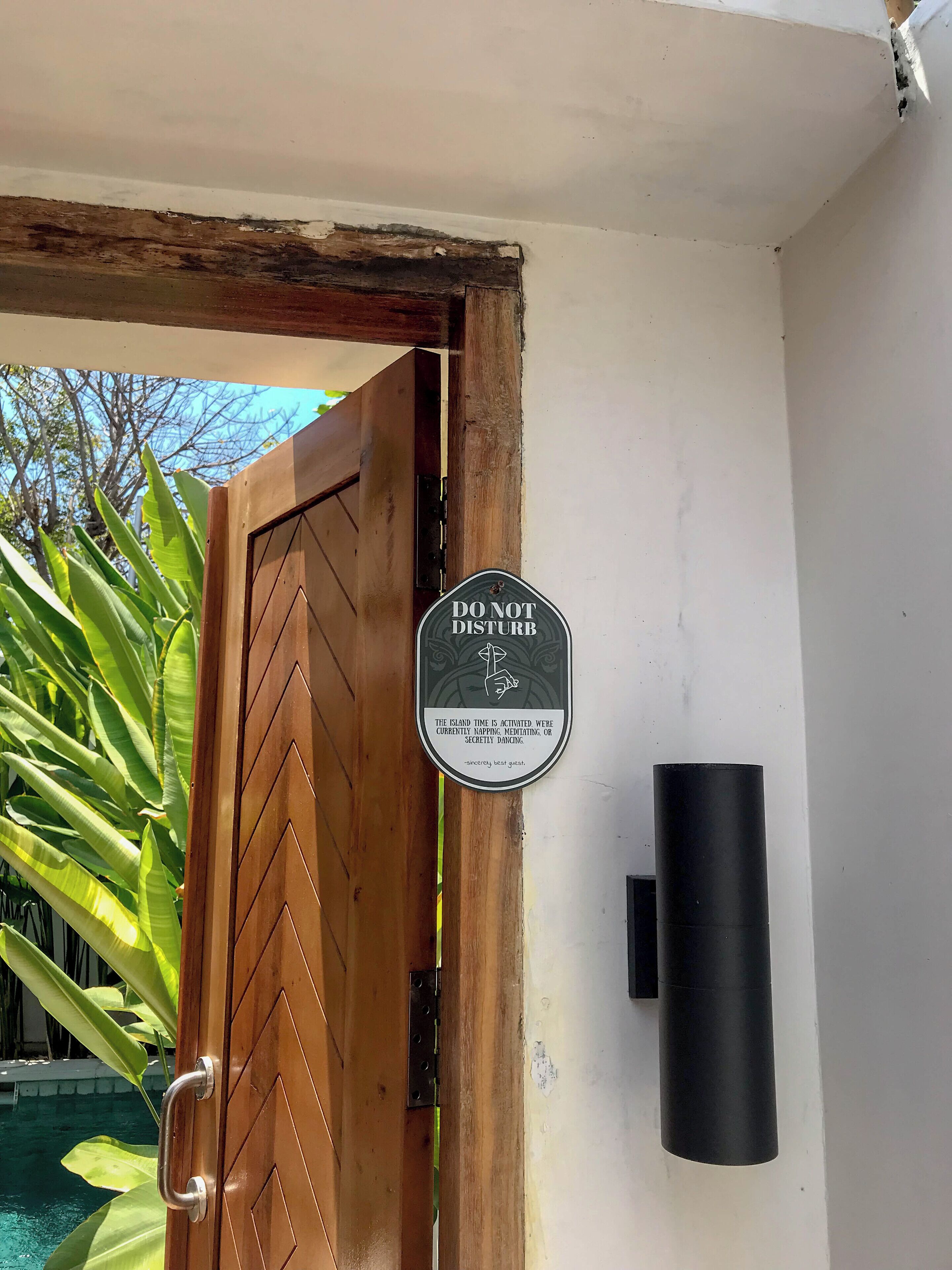Een houten deur met een 'DO NOT DISTURB' bordje, een metalen handgreep en een zwart, cilindrisch object aan de muur.