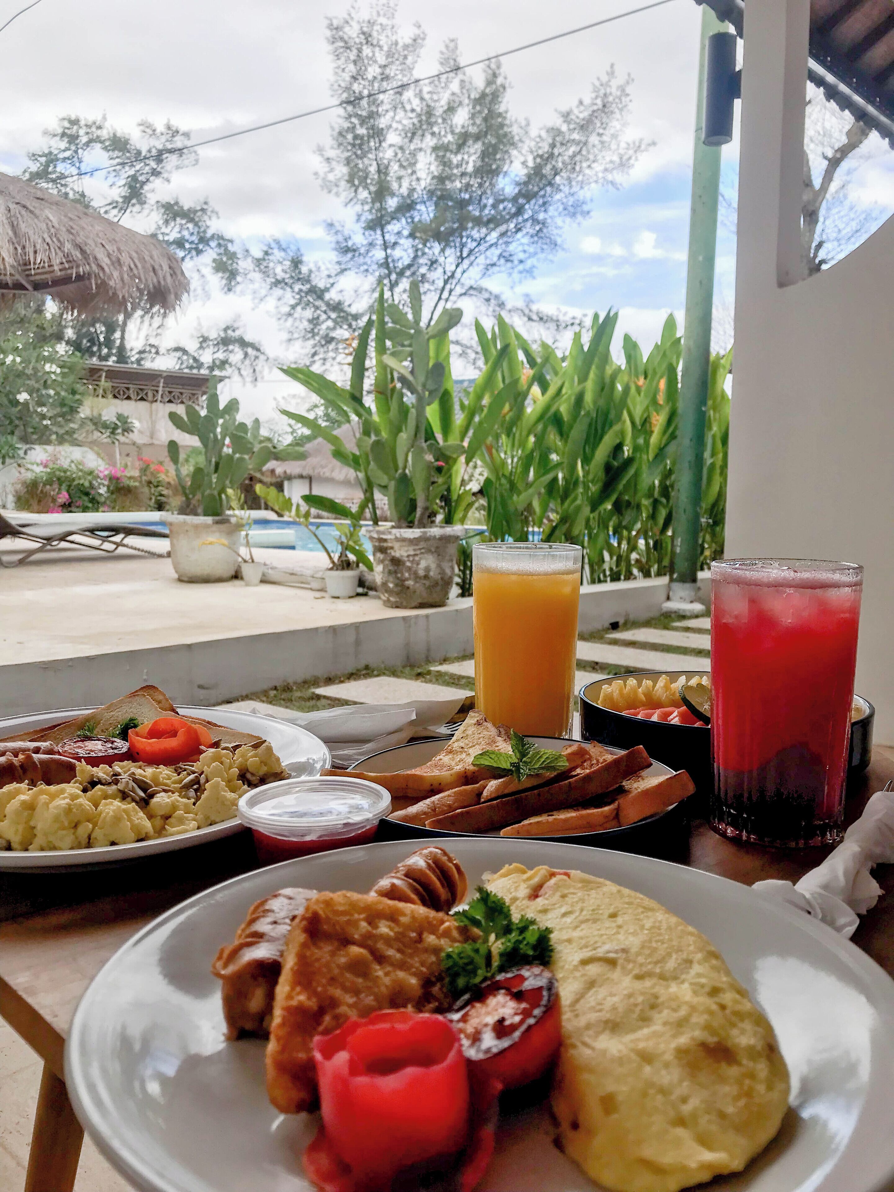 Una mesa de desayuno con diversos platos, un vaso de jugo de naranja y un vaso de jugo rojo.