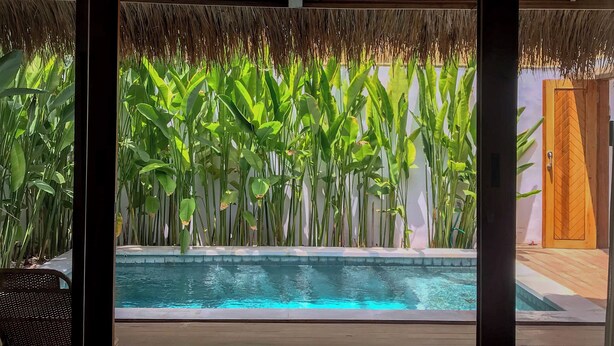 A poolside area with a view of a swimming pool, surrounded by lush greenery and a thatched roof structure. - RATU Village – Luxury Island Apartment & Private Villa Gili Air (Gili Air)