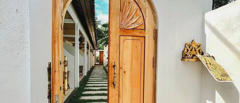 A wooden door with a decorative archway leading to a covered outdoor area with a tiled floor.