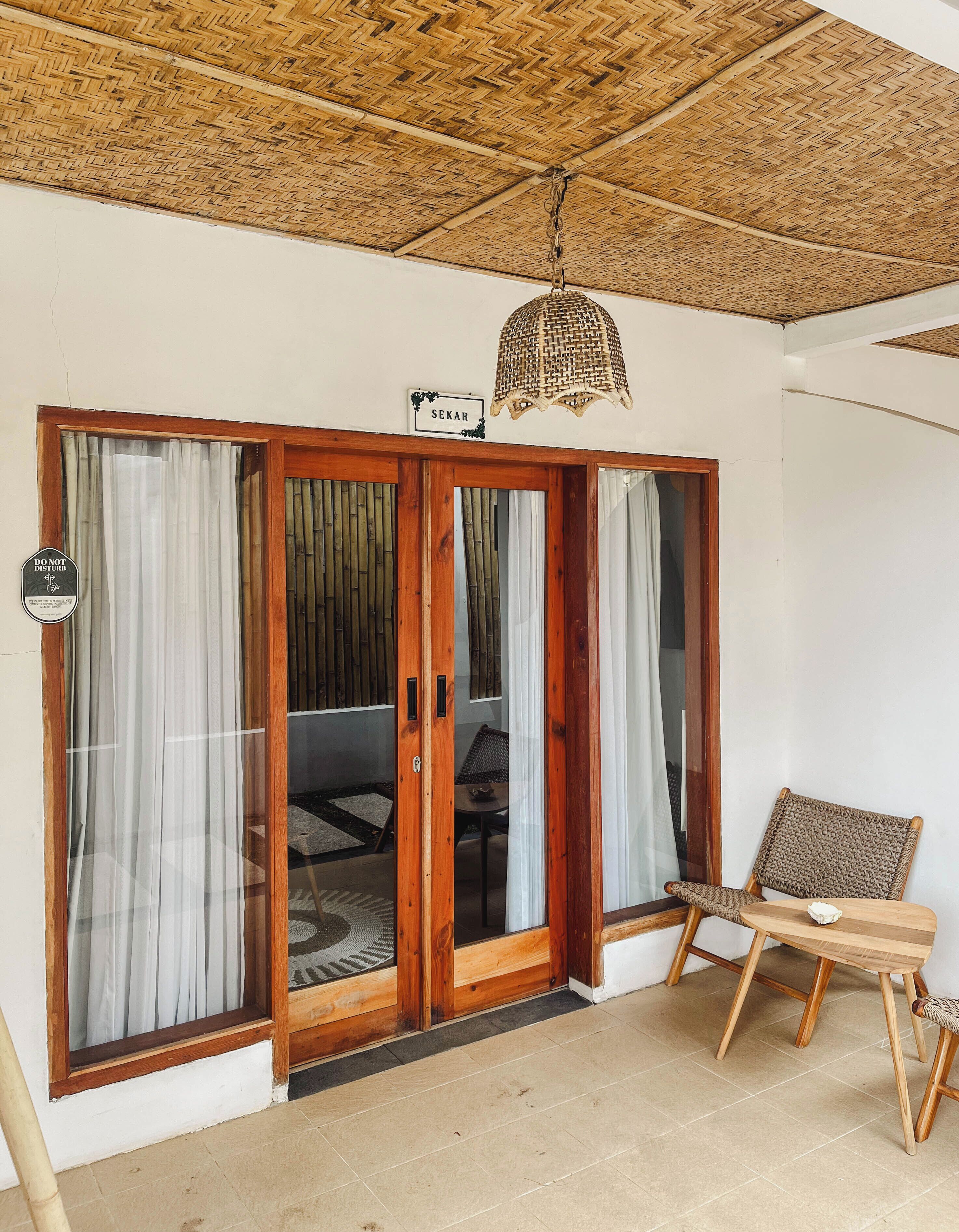 A room with a woven ceiling, a sliding glass door with a 'DO NOT DISTURB' sign, a wicker chair, and a small table.