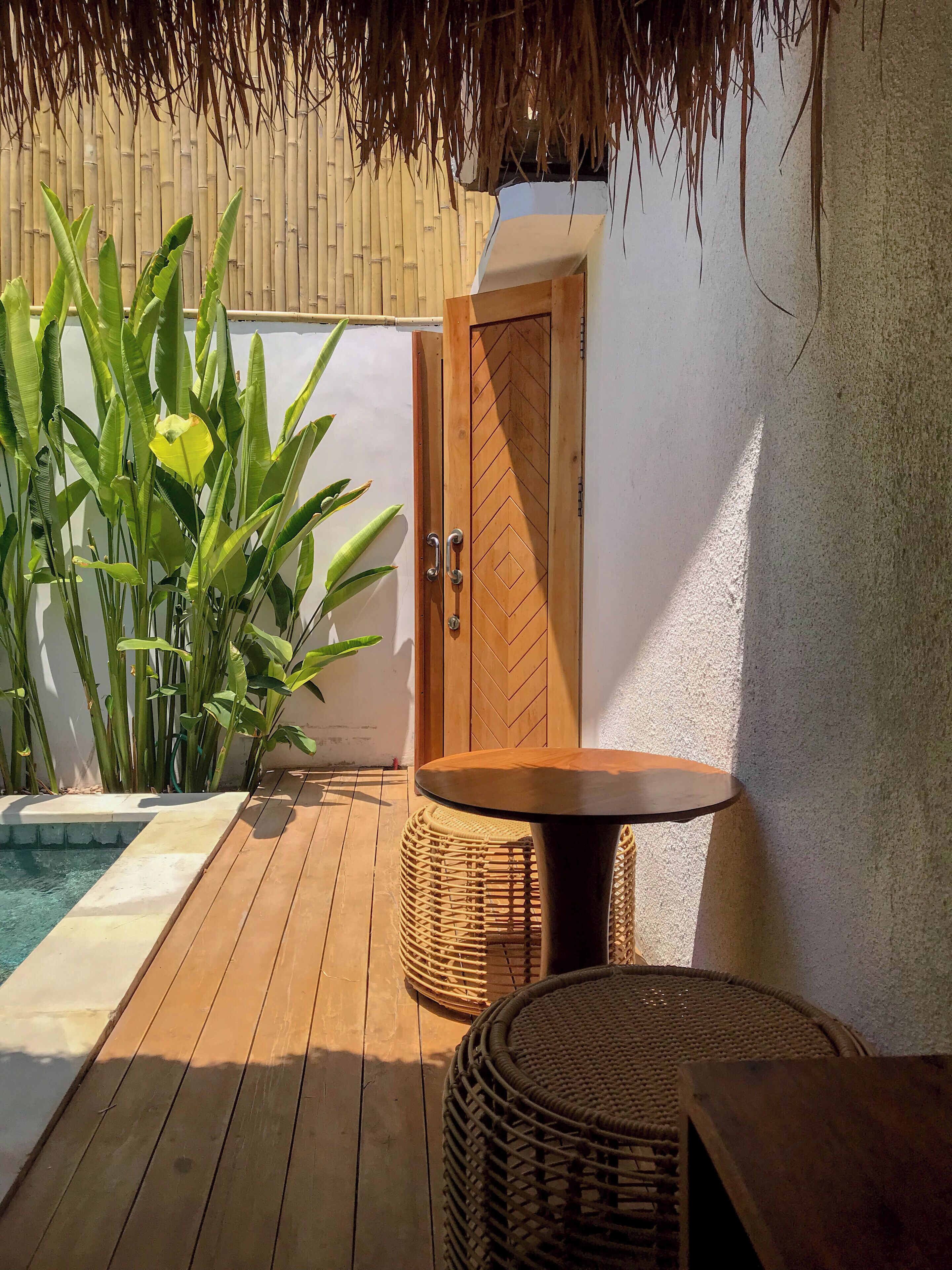 A wooden deck with a pool, a wicker table, and a door with a geometric pattern.