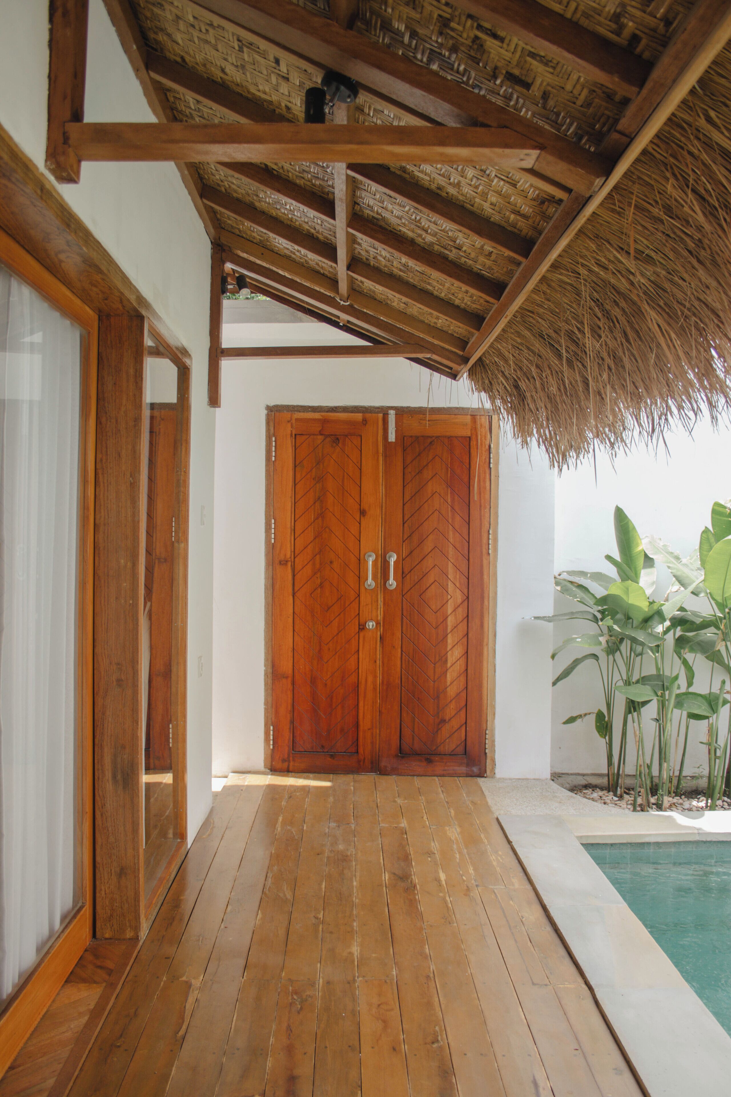 A wooden door with a herringbone pattern, leading to a pool area with a thatched roof and wooden beams.