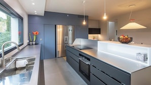A modern kitchen with a built-in oven, a stainless steel refrigerator, and a large island with a bowl of fruit.