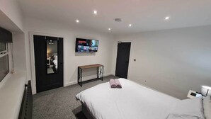 Une chambre d’hôtel avec un lit, un téléviseur fixé au mur, une petite table et une porte.