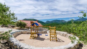 A playground with a swing set and a slide, surrounded by a stone wall and a view of mountains.