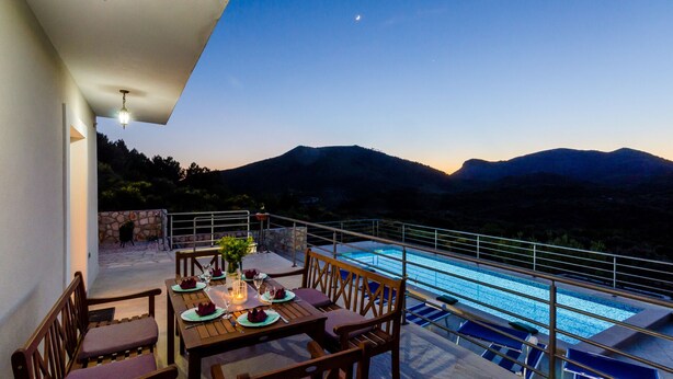 A dining area with a table set for four, overlooking a swimming pool and mountains.