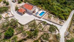 An aerial view of a property with a swimming pool, a patio area, and a stone wall.