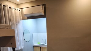 Ein kleines Zimmer mit Etagenbett, Tisch mit Stühlen, Waschbecken und Spiegel.