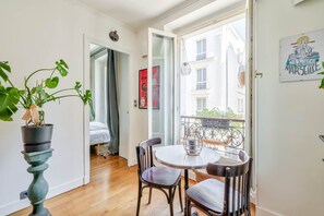A room with a dining table and chairs, a potted plant, a bed with a curtain, and a balcony with a railing.