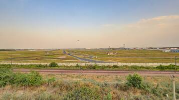 A wide view of an airport runway with multiple aircraft, airport buildings, and surrounding fields.