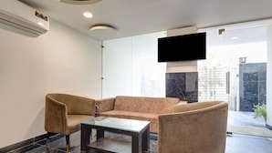 A modern living room with a beige sofa, a glass coffee table, and matching armchairs. A flat-screen TV is mounted on the wall. - Mauryan Signature hotel with Airport View (New Delhi)