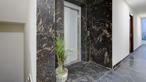 A hallway with dark marble walls, a white door, and a potted plant. - Mauryan Signature hotel with Airport View (New Delhi)