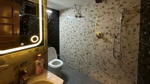 A modern bathroom with a large mirror, a toilet, a shower with a handheld showerhead, and a soap dispenser on the sink. - Desire Courtyard (New Delhi)