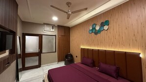 A bedroom with a bed, a ceiling fan, a wall-mounted air conditioner, and a decorative wall panel. - Desire Courtyard (New Delhi)
