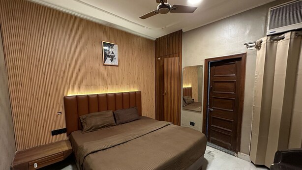 A bedroom with a bed, a wooden headboard, a ceiling fan, a wardrobe, and a mirror. - Desire Courtyard (New Delhi)