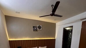 A bedroom with a bed, wooden headboard, ceiling fan, and a small air conditioning unit. - Desire Courtyard (New Delhi)