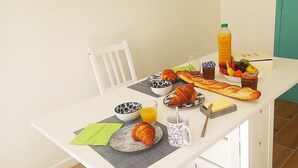 Ein Frühstückstisch mit Croissants, einer Baguette, einer Obstschale, einer Orangensaftflasche und einem Glas Orangensaft.