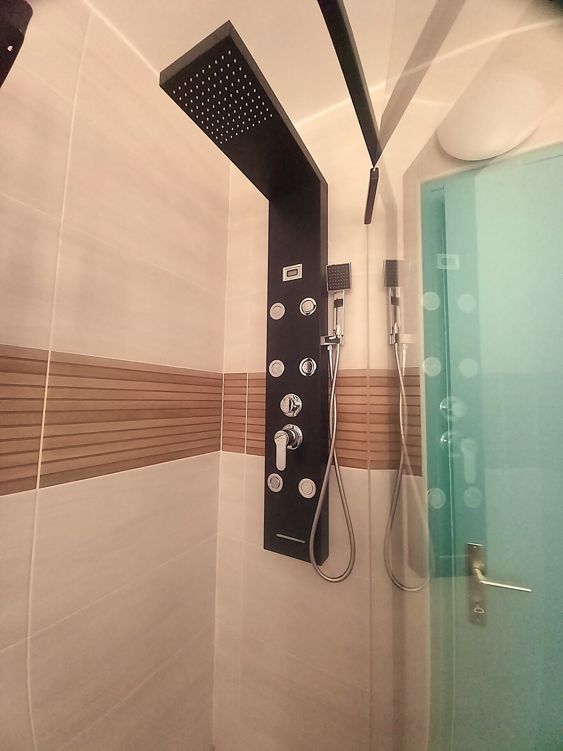 Een moderne badkamer met een douche, een glazen deur en een bedieningspaneel met verschillende standen.