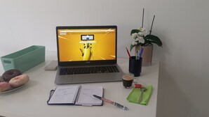 Ein Laptop auf einem Schreibtisch zusammen mit einem Notizbuch, einem Stift, einer Kaffeetasse und einem Teller mit Donuts.