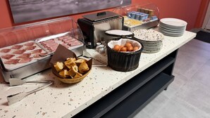 A buffet setup with various food items, including meats, eggs, and bread, arranged on a countertop. - Hotel du Village (Village-Neuf)