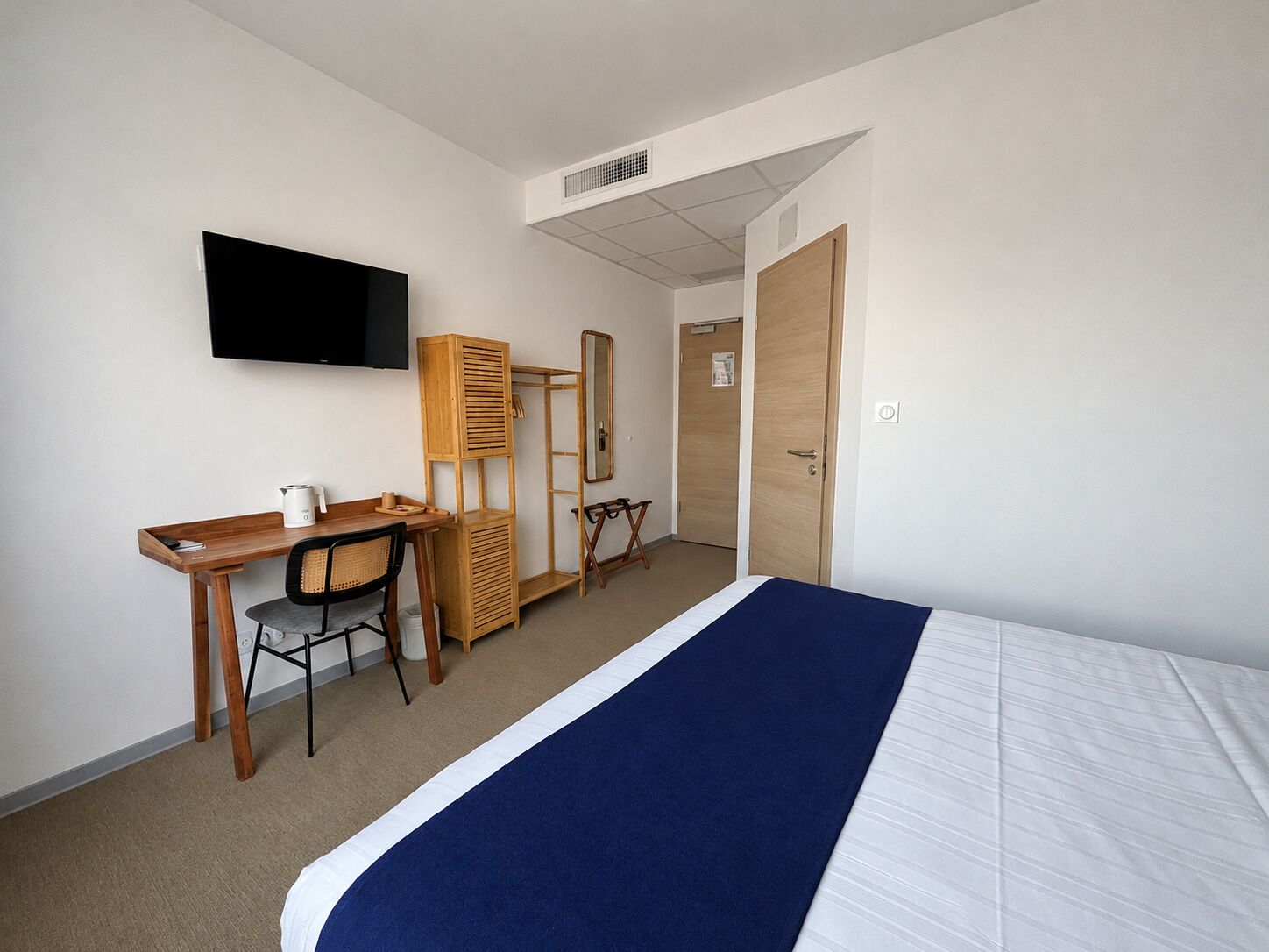 A hotel room with a bed, a desk, a chair, a television, and a wardrobe.