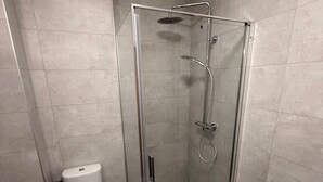 A modern bathroom with a glass-enclosed shower, a toilet, and tiled walls. - Hotel du Village (Village-Neuf)