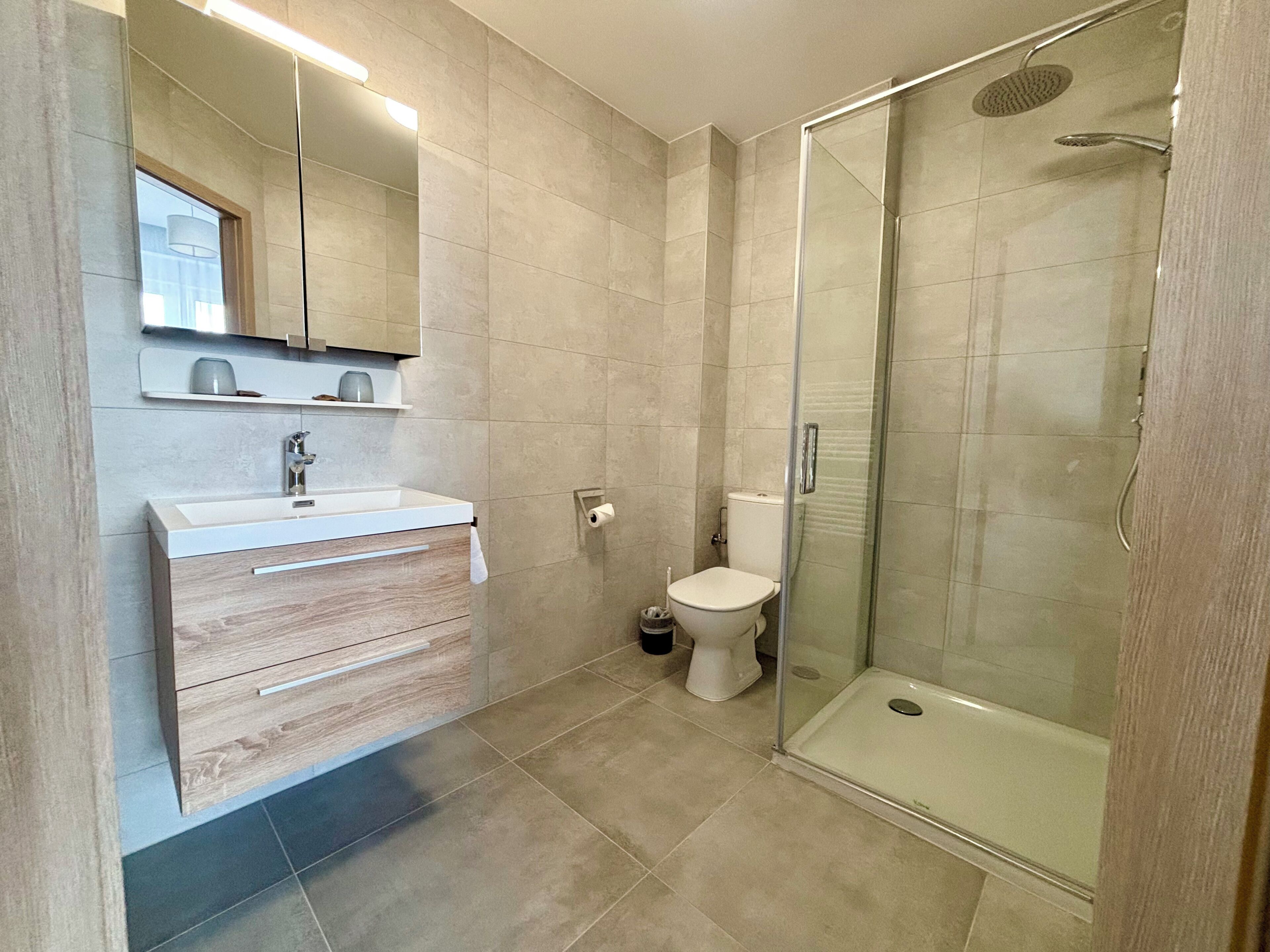 Un baño moderno con cabina de ducha de vidrio, un lavabo blanco con espejo arriba y un inodoro.
