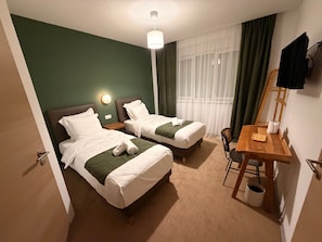 Et hotelværelse med to senge, et skrivebord, en stol, en lampe og et vindue med gardiner.