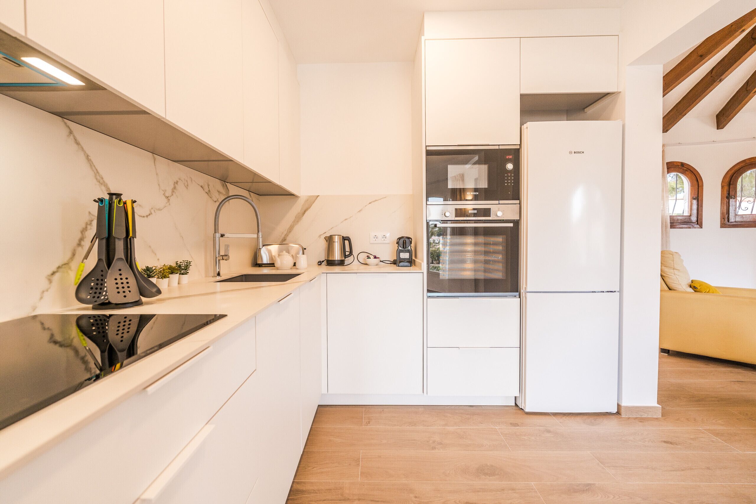 Una cocina moderna con armarios blancos, un refrigerador Bosch, horno empotrado y placa de inducción negra.