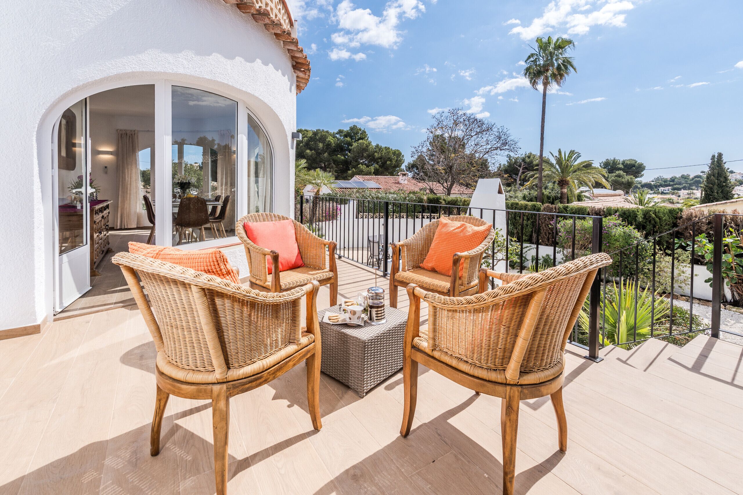 A balcony with wicker chairs, a table, and a view of a residential area.