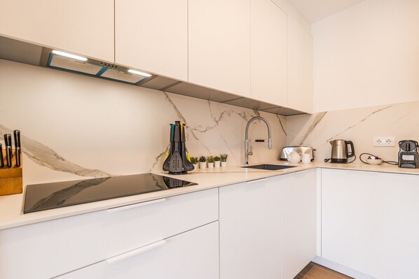 A modern kitchen with white cabinets, a black induction cooktop, a stainless steel kettle, and a coffee maker.