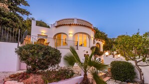 A white building with a curved balcony, arched windows, and a stone pathway leading to the entrance. - Casa Golondrina (Moraira)