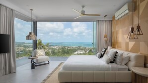A modern bedroom with a large bed, a sofa, a TV, and a view of the ocean.